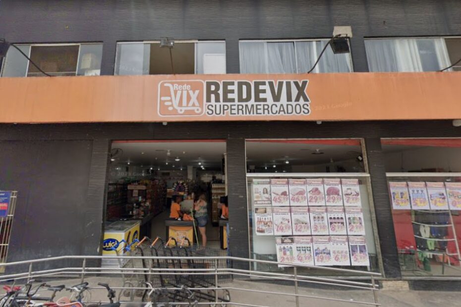 Fachada do Supermercado Rede Vix Jabaeté em Vila Velha. A imagem mostra a entrada principal com a placa "Rede Vix Supermercados", as vitrines com anúncios de ofertas e um carrinho de compras na frente da loja.